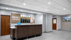 A reception area with a wooden reception desk, a 'Welcome to Hampton' sign, and a 'Hilton' sign. - Hampton Inn Lexington Medical Center (Lexington)