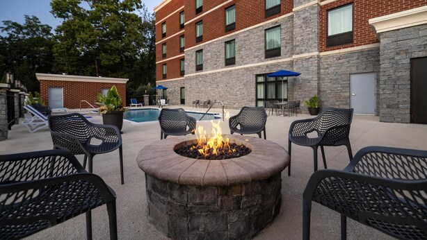 A courtyard with a stone fire pit surrounded by outdoor seating, a pool, and a multi-story building with brick and stone facade. - Hampton Inn Lexington Medical Center (Lexington)