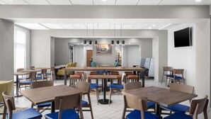 A modern dining area with multiple tables and chairs, a central light fixture, and a television on the wall. - Hampton Inn Lexington Medical Center (Lexington)