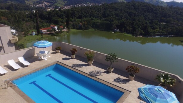 A swimming pool with lounge chairs and umbrellas, surrounded by potted plants and overlooking a lake. - Hotel Central Parque (Sao Lourenco)