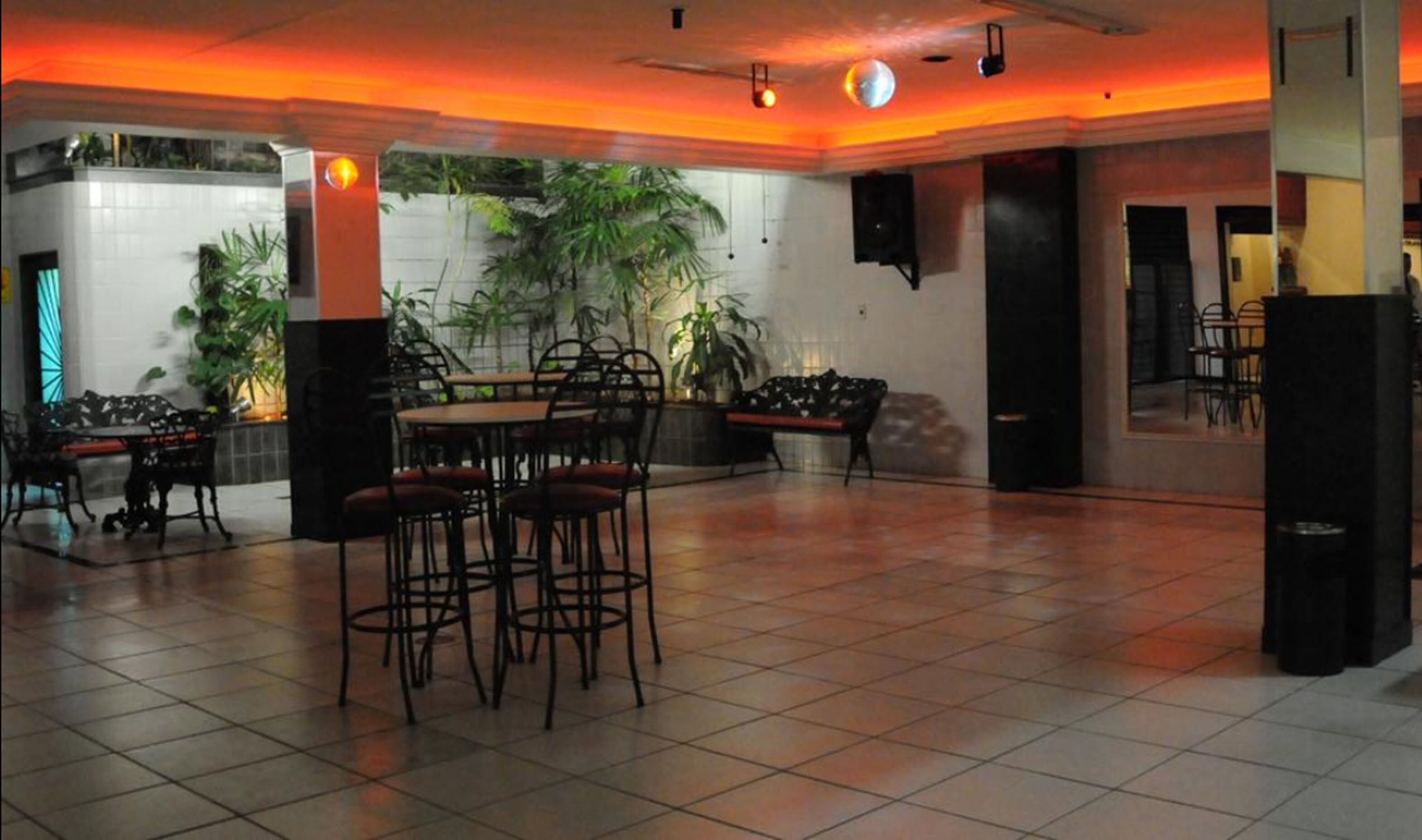 A spacious indoor area with a tiled floor, a round table with chairs, and several potted plants.