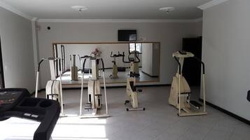 Uma academia com equipamentos de cardio, máquinas de peso e um painel de espelhos.