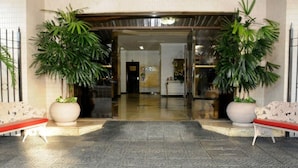 A hotel entrance with a tiled floor, two large potted plants, and a bench. - Hotel Central Parque (Sao Lourenco)