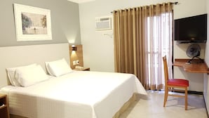 A hotel room with a large bed, a desk with a chair, a television, and a window with curtains. - Hotel Central Parque (Sao Lourenco)