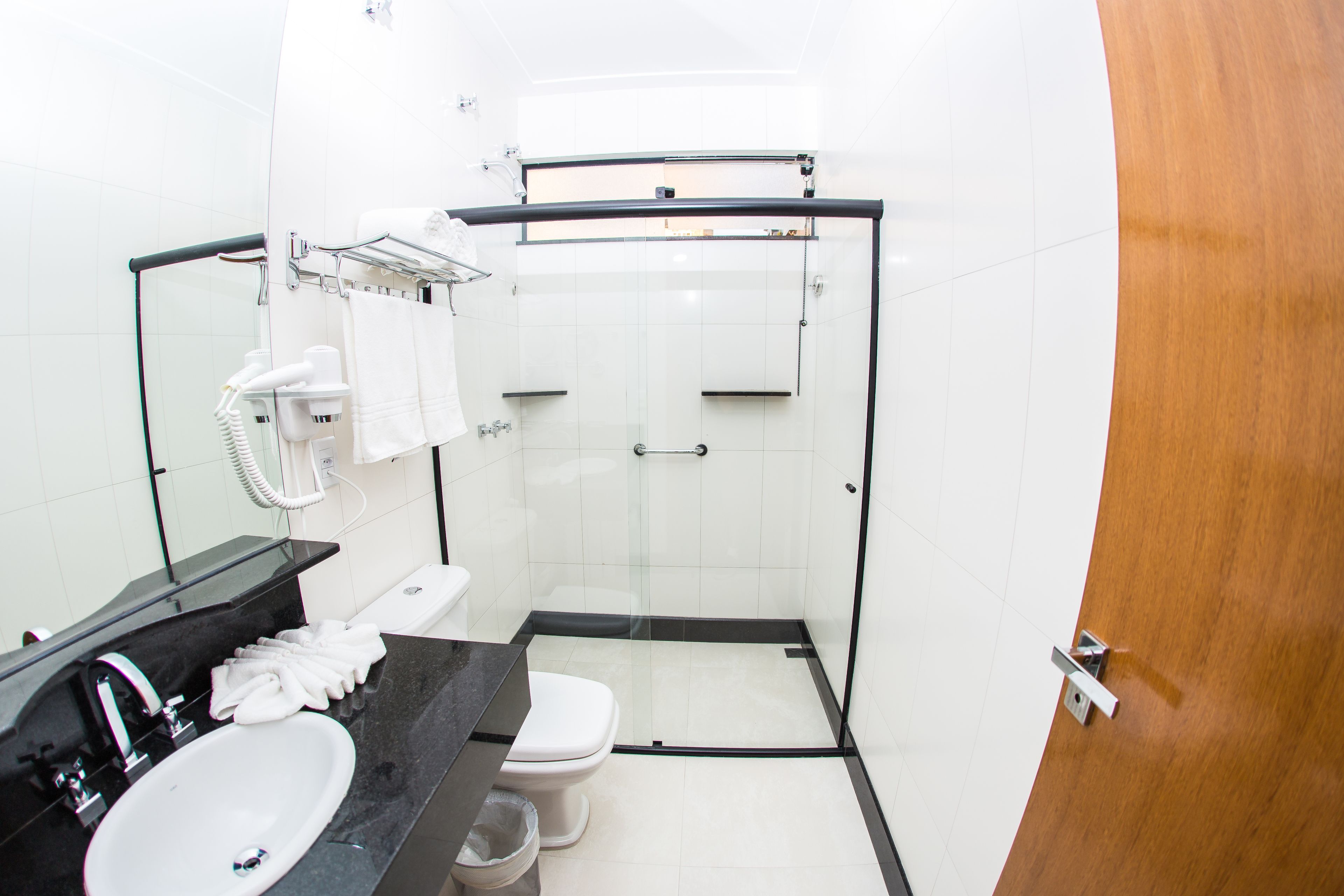 Un baño moderno con cabina de ducha de vidrio, encimera negra con lavabo y un inodoro blanco.