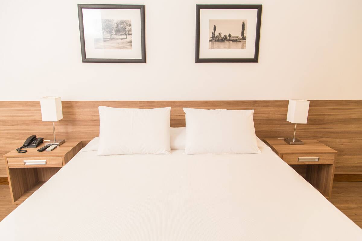 A hotel room with a large bed, two bedside tables with lamps, a phone, and a drawer.