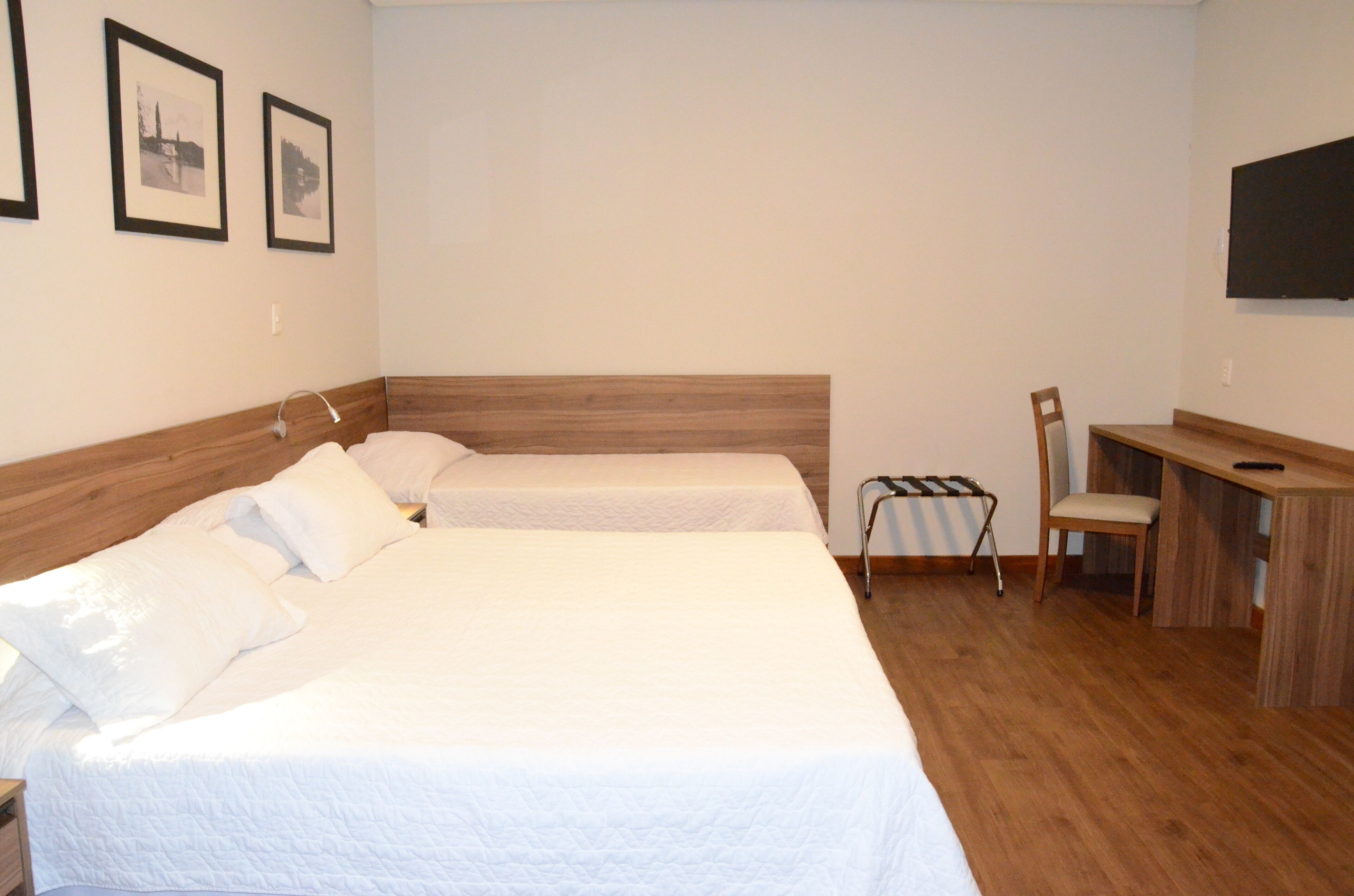 A bedroom with two beds, a desk, a chair, and a TV on the wall.