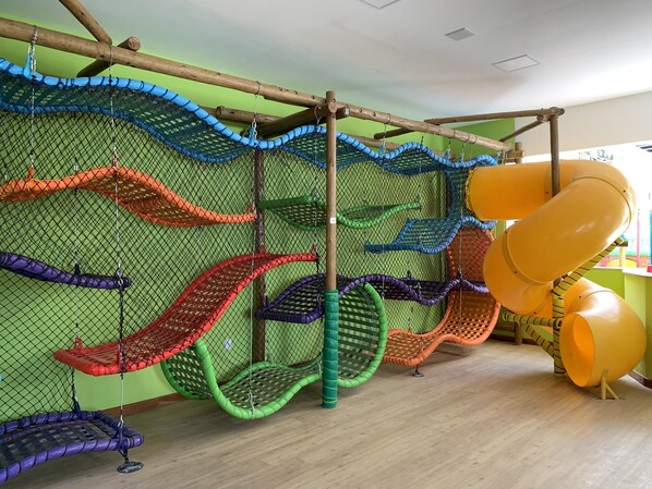 A play area with multiple slides and swings, enclosed by a netted fence. - Hotel Metropole (Sao Lourenco)