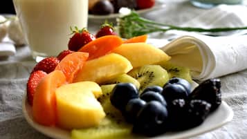 A plate of assorted fresh fruits including strawberries, blueberries, kiwi, and mango slices, with a glass of milk in the background.