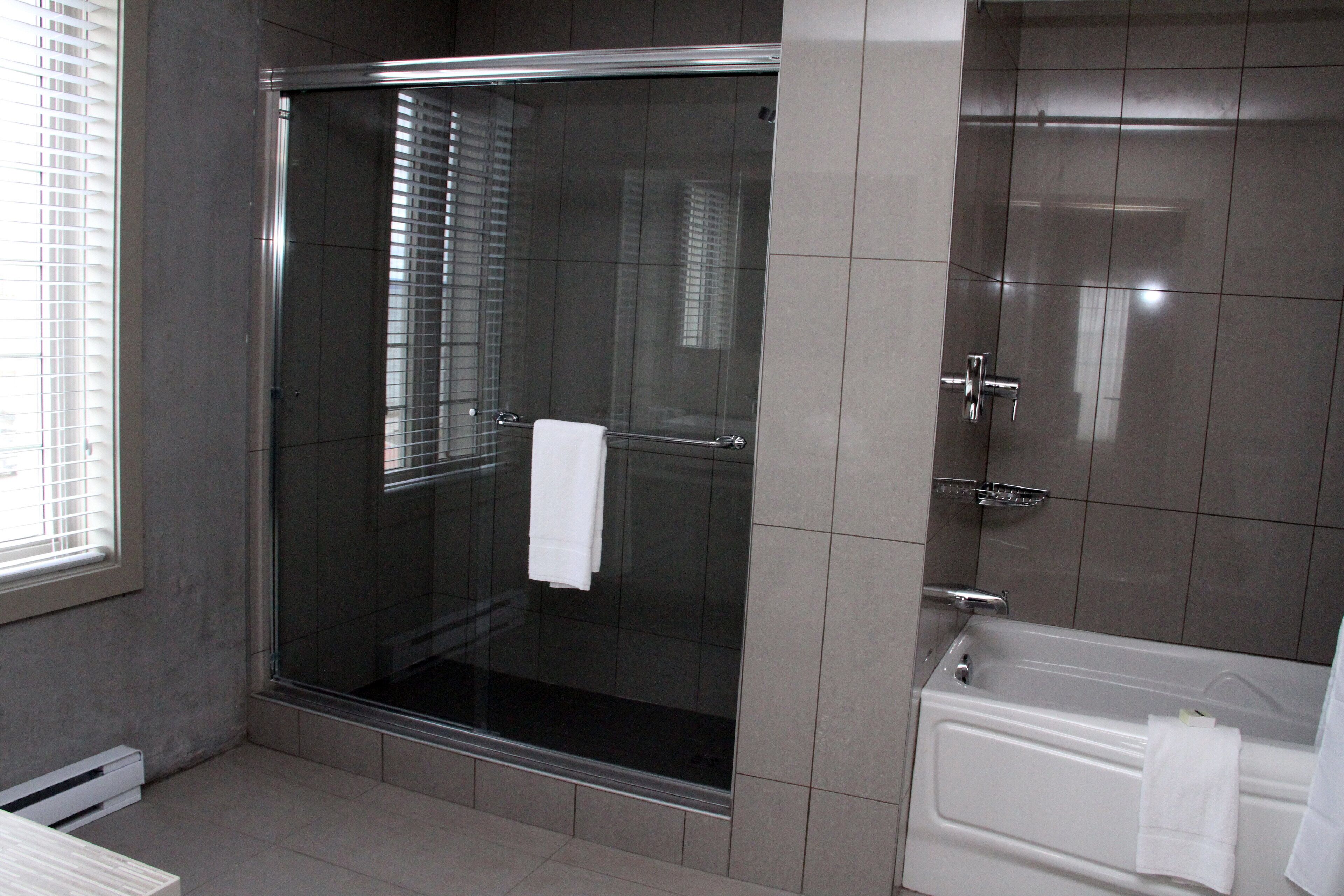Un baño moderno con ducha de vidrio, bañera blanca y ventana con persianas.