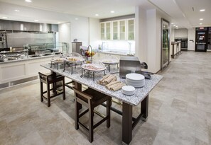 A modern kitchen with granite countertops, stainless steel appliances, and a glass-enclosed dining area with a buffet setup.