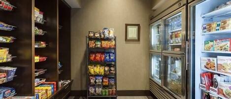 Un pasillo de hotel con estantes para aperitivos, un refrigerador y un cuadro en la pared.