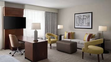 A hotel room with a desk, two armchairs, a sofa, and a TV.