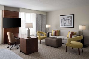 A hotel room with a desk, two armchairs, a sofa, and a TV.