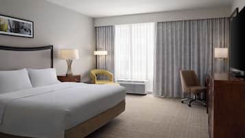 A hotel room with a large bed, two bedside lamps, a desk, a chair, and a large window with curtains.