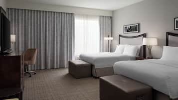 A hotel room with two beds, a desk, a chair, and a large window with curtains.