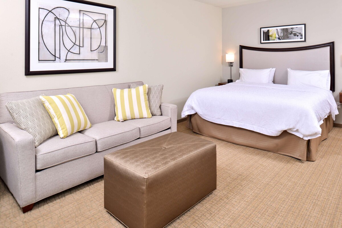 A hotel room with a bed, a sofa, and a small ottoman.