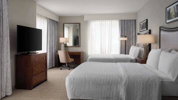 A hotel room with a large bed, a TV on a wooden dresser, a desk with a chair, and two bedside lamps.