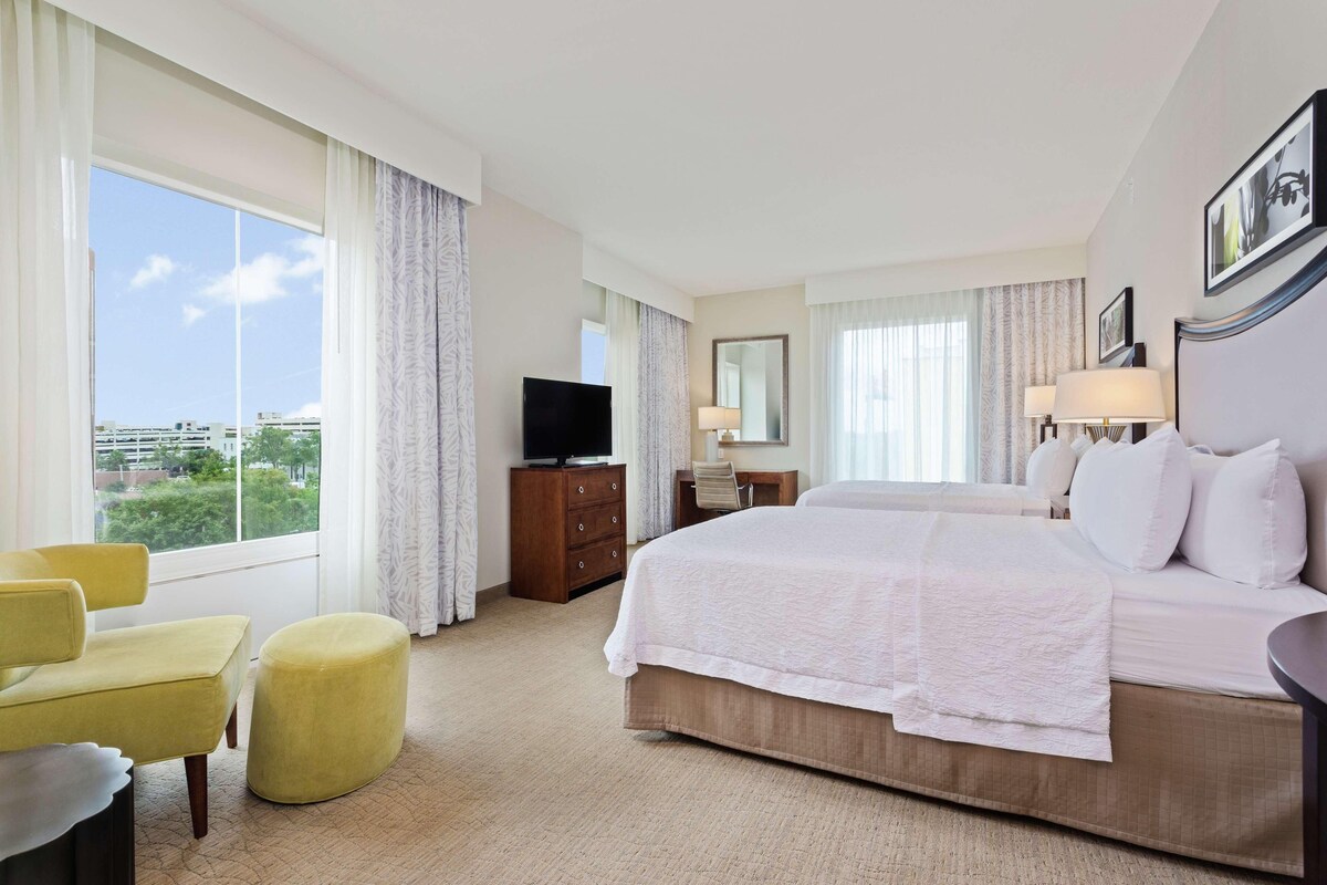 A hotel room with a large bed, a desk, a chair, a television, and a view of the city.