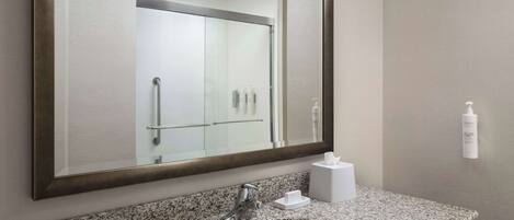 A bathroom with a granite countertop, a white sink, a large mirror, and a hand dryer.