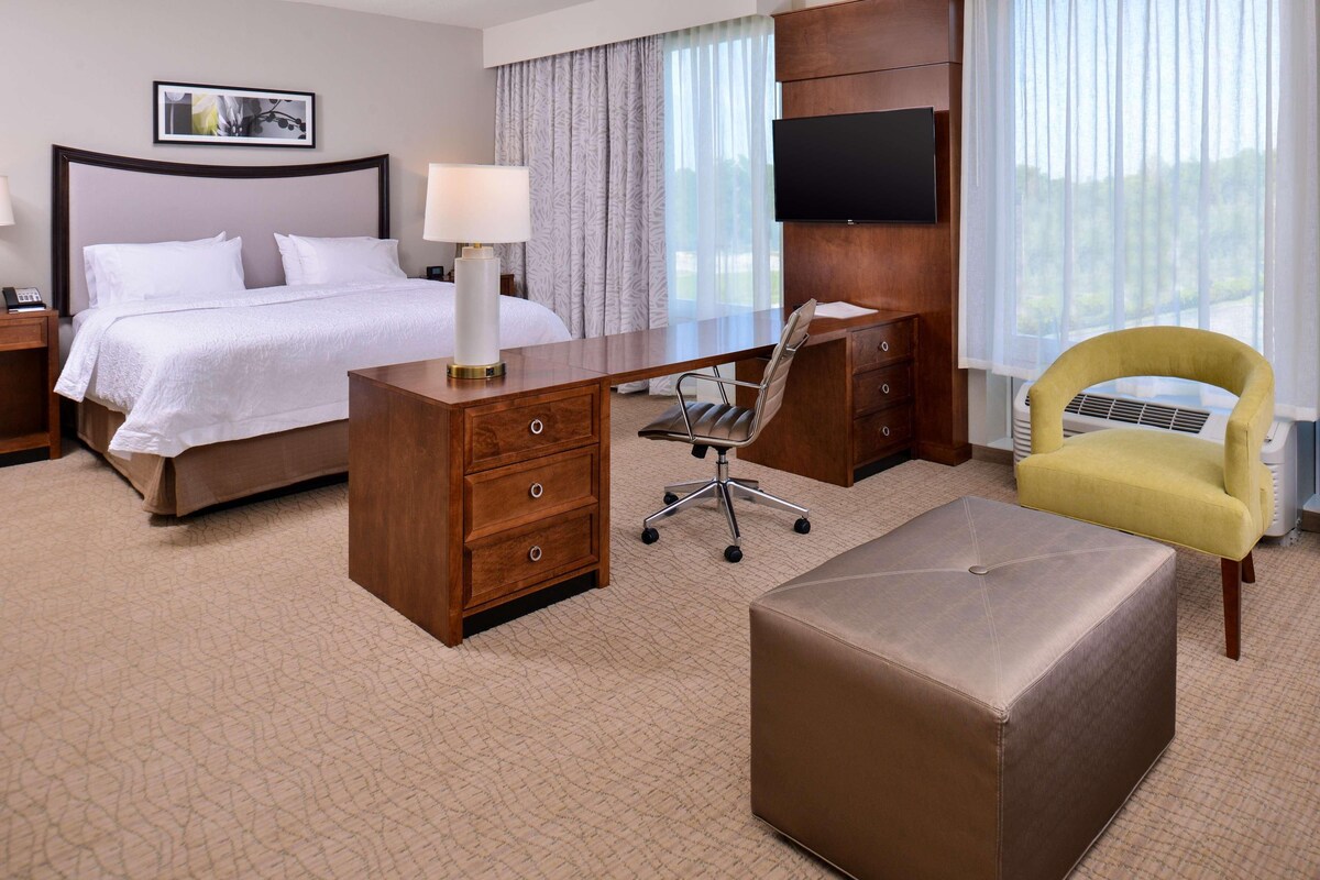 A hotel room with a bed, a desk, a chair, a TV, and a window with curtains.