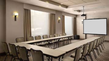 A conference room with a long table, chairs, a projector screen, and wall-mounted lamps.