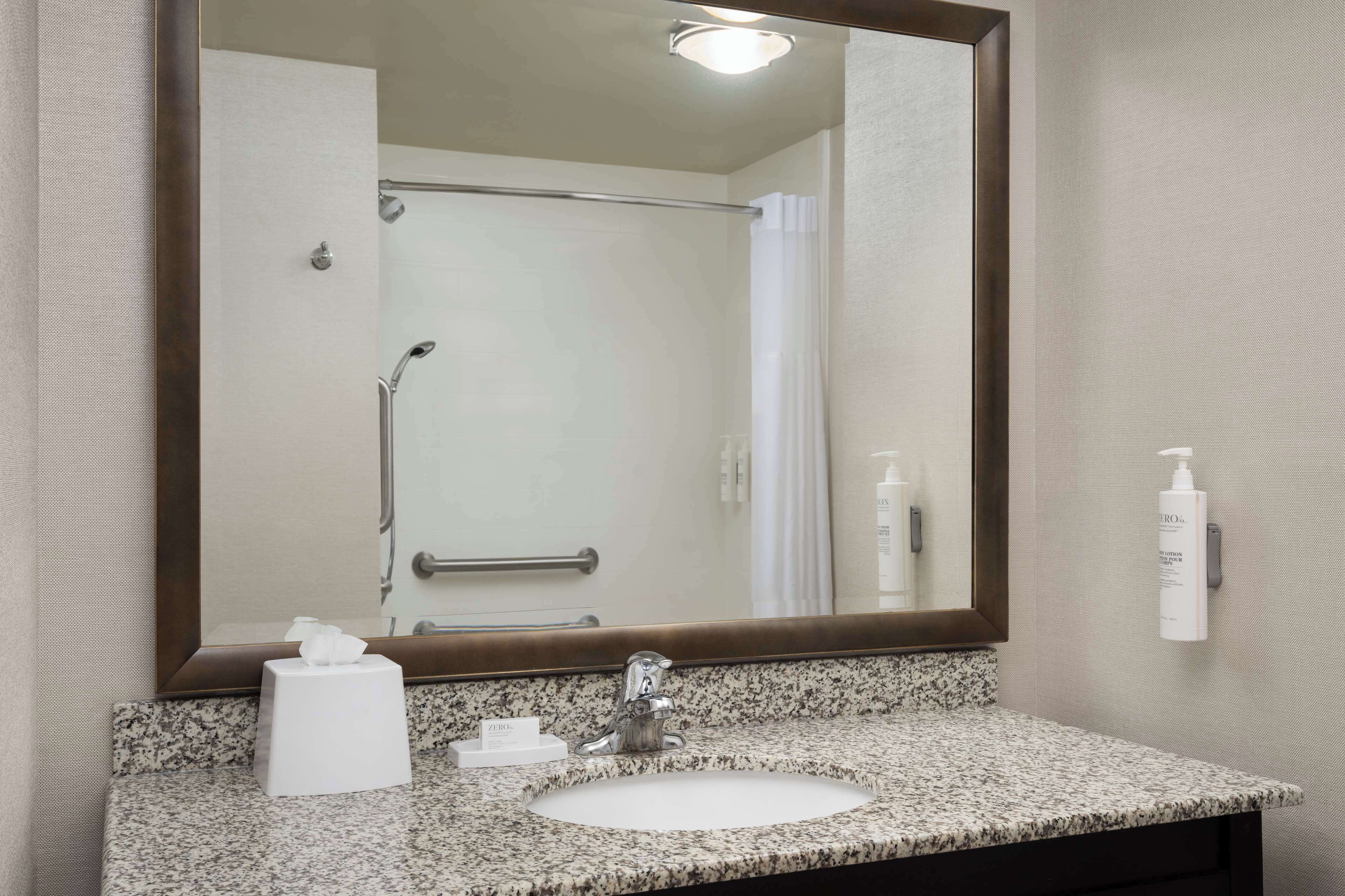 A bathroom with a granite countertop sink, a large mirror, a towel rack, and a shower with a glass door.