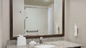 A bathroom with a granite countertop sink, a large mirror, a towel rack, and a shower with a glass door.
