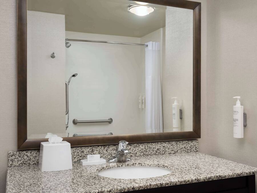 A bathroom with a granite countertop sink, a large mirror, a towel rack, and a shower with a glass door.