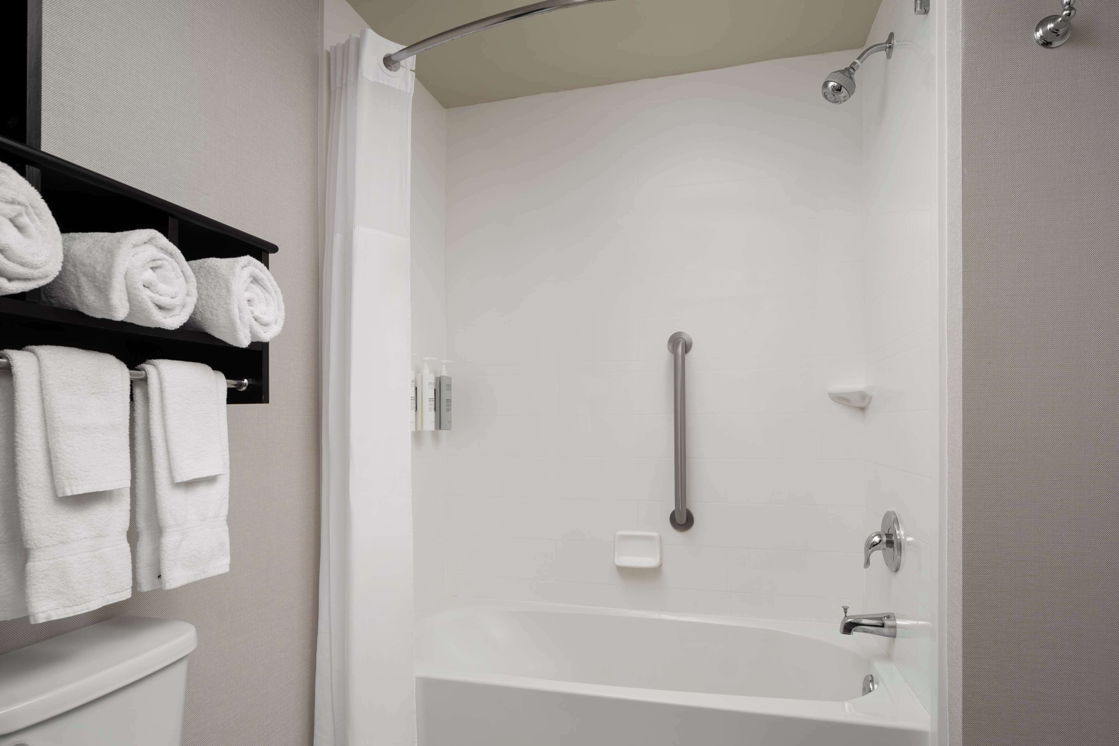 A modern bathroom with a bathtub, a toilet, and a shelf with neatly folded towels.