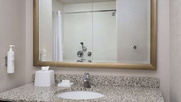 Un baño con un espejo grande, un lavabo, un dispensador de toallas y una zona de ducha.