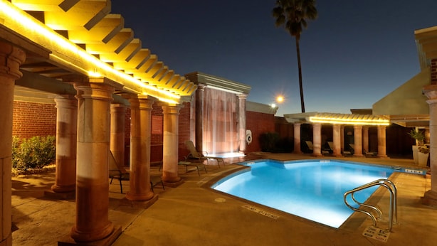 Un área de piscina con columnas, una pérgola y una palmera.