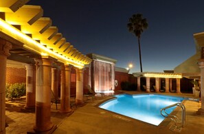 Un área de piscina con columnas, una pérgola y una palmera.