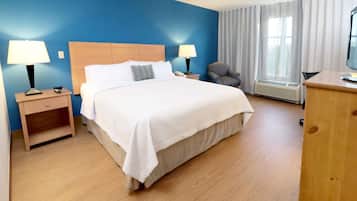 Une chambre d’hôtel avec un grand lit, deux tables de chevet avec des lampes, une chaise, un bureau avec un ordinateur et une fenêtre avec des rideaux.