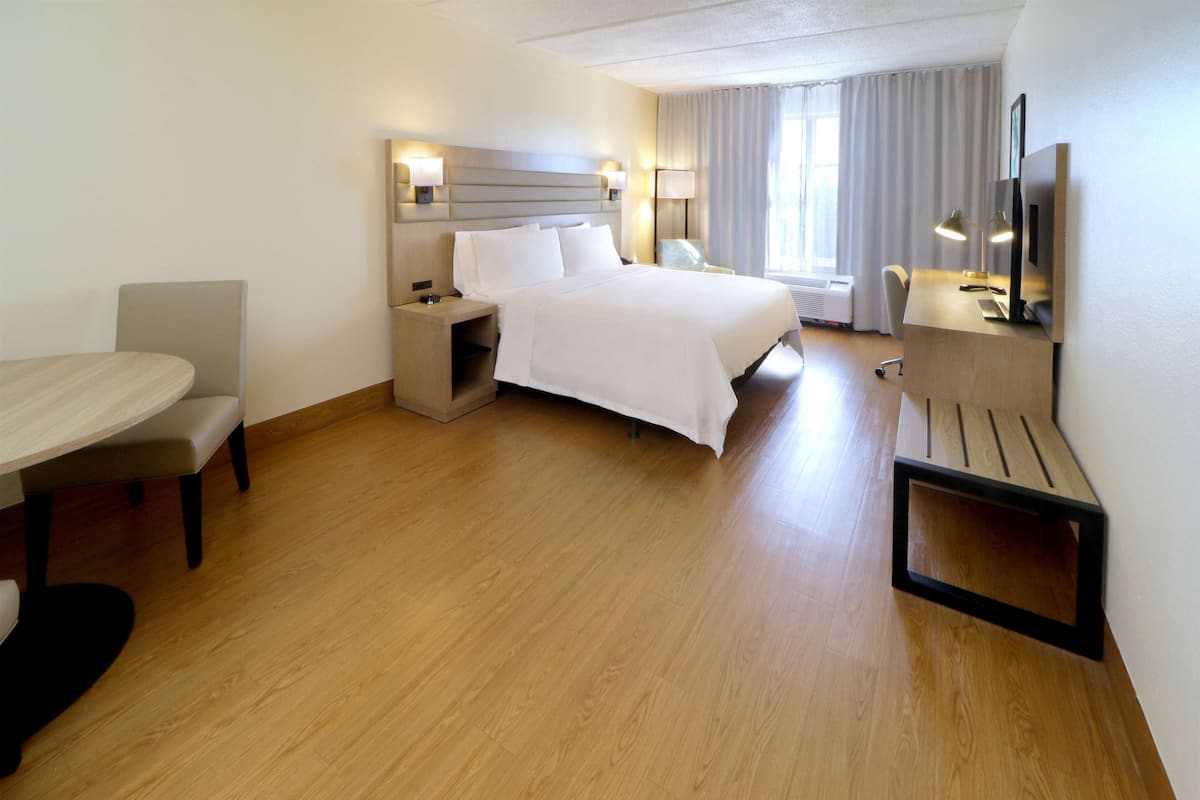 A hotel room with a bed, bedside tables, a desk, a chair, and a TV.