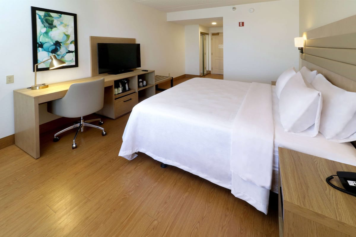 A hotel room with a bed, a desk with a chair, a television, and a painting on the wall.