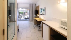 Una habitación de hotel moderna con escritorio, silla, televisor y balcón con mobiliario exterior.
