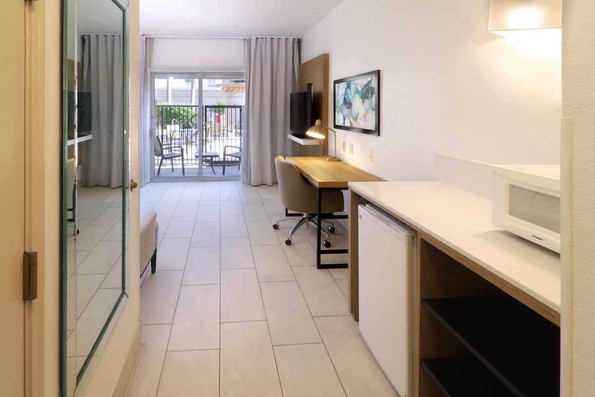 A modern hotel room with a desk, chair, TV, and a balcony with outdoor seating.