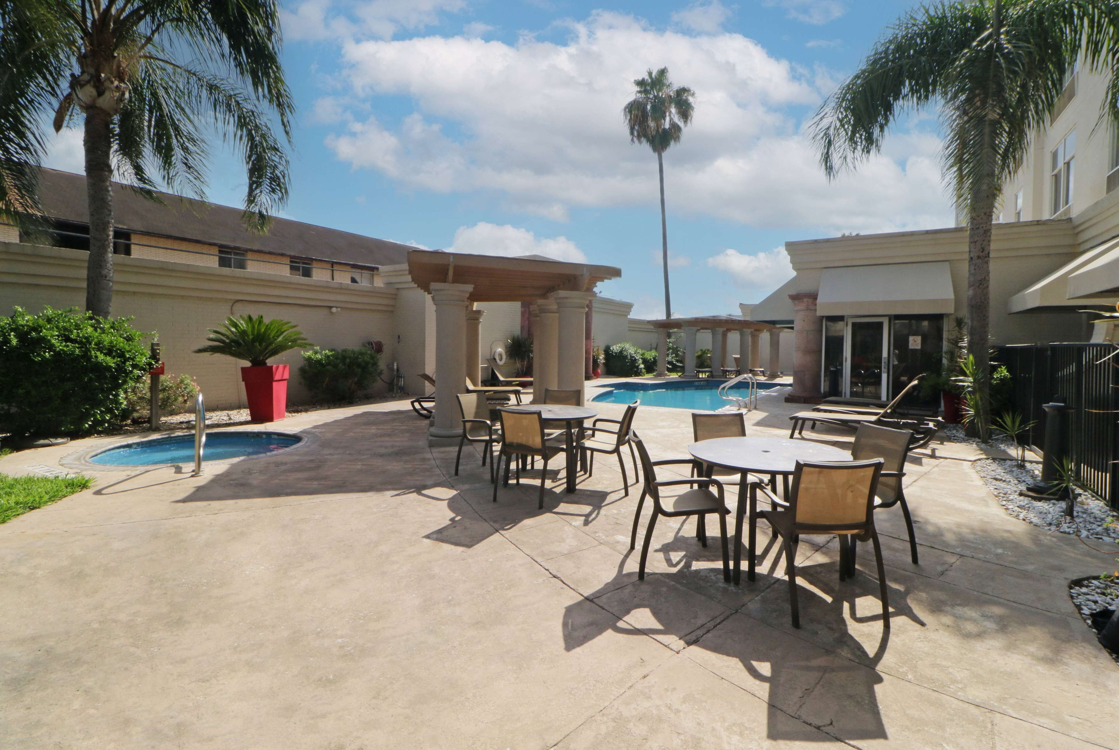 An outdoor patio with a pool, seating, and palm trees.