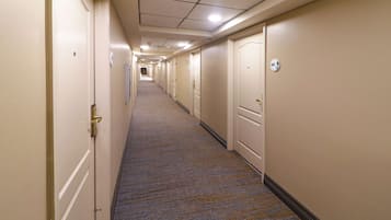 A long, narrow hotel corridor with carpeted floors and doors on both sides.