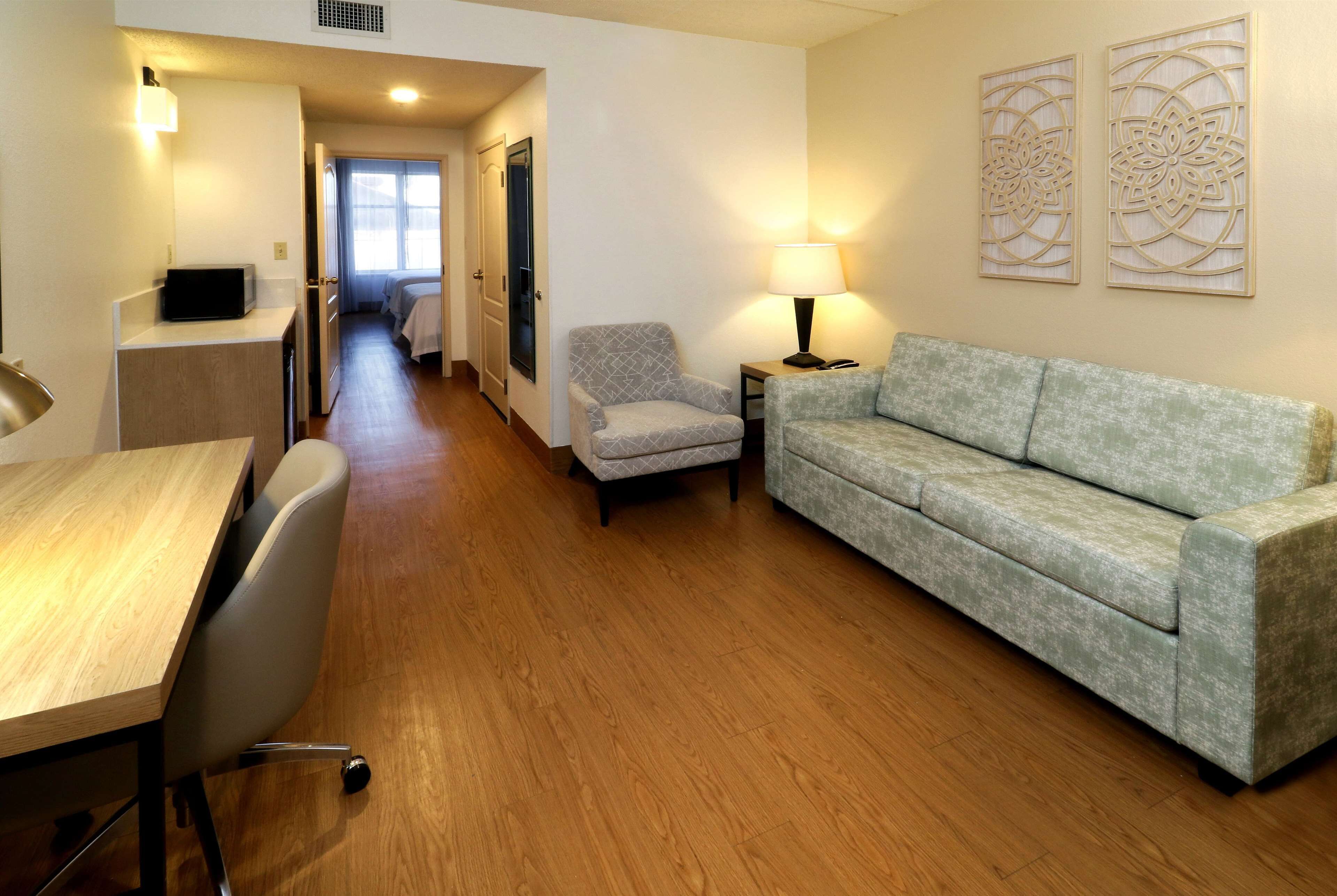 A hotel room with a wooden floor, a sofa, a chair, a desk, and a lamp.