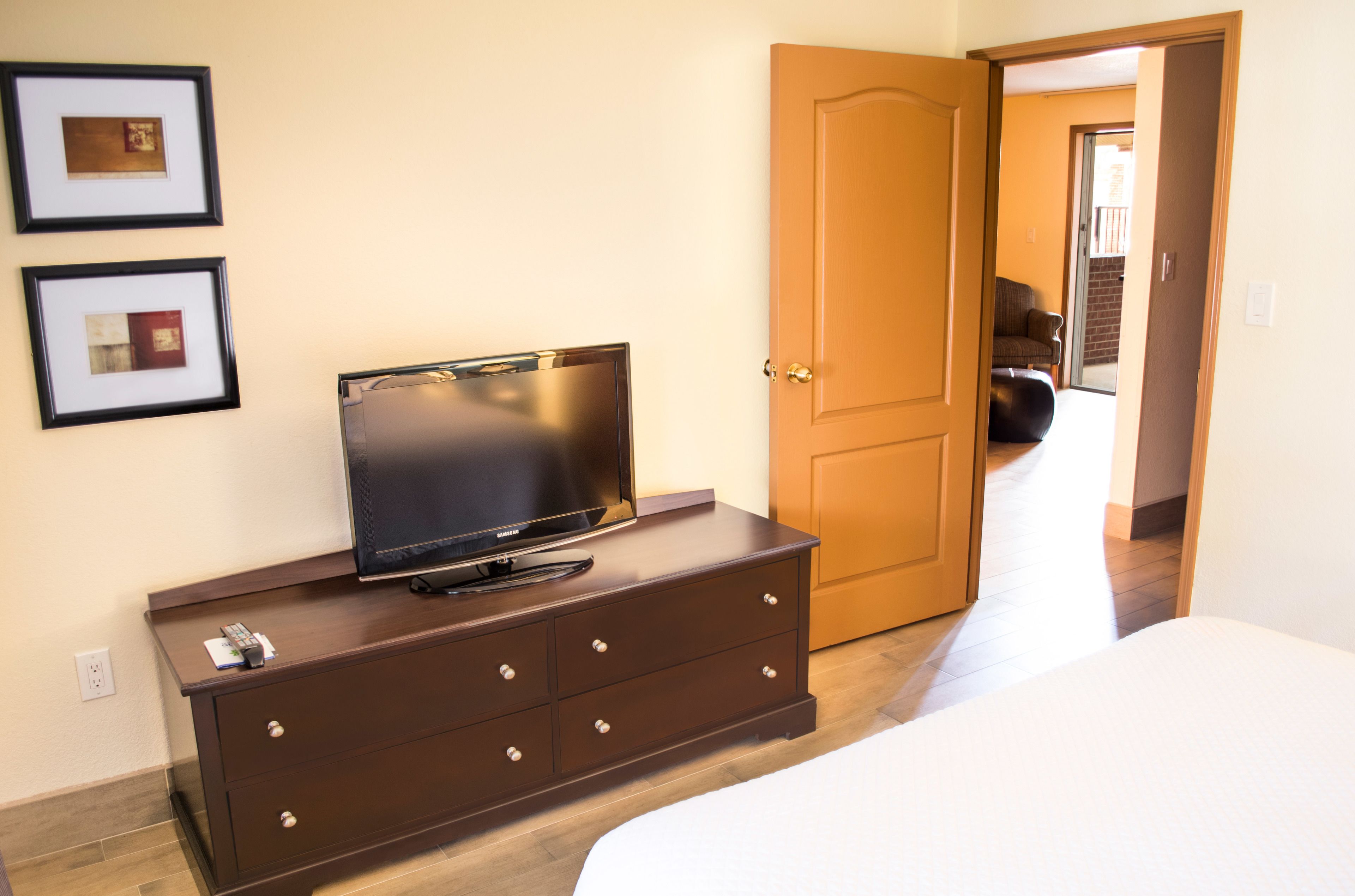 A bedroom with a TV on a dresser, a door to a living area, and a bed.