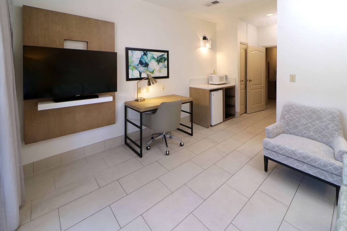 A modern living room with a flat-screen TV, a desk with a chair, a microwave, and a sofa.