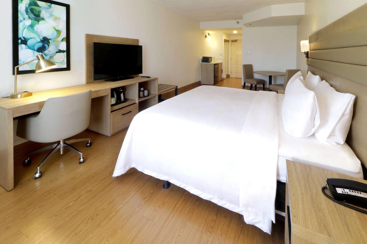 A hotel room with a bed, desk, chair, television, and a small table with a lamp.