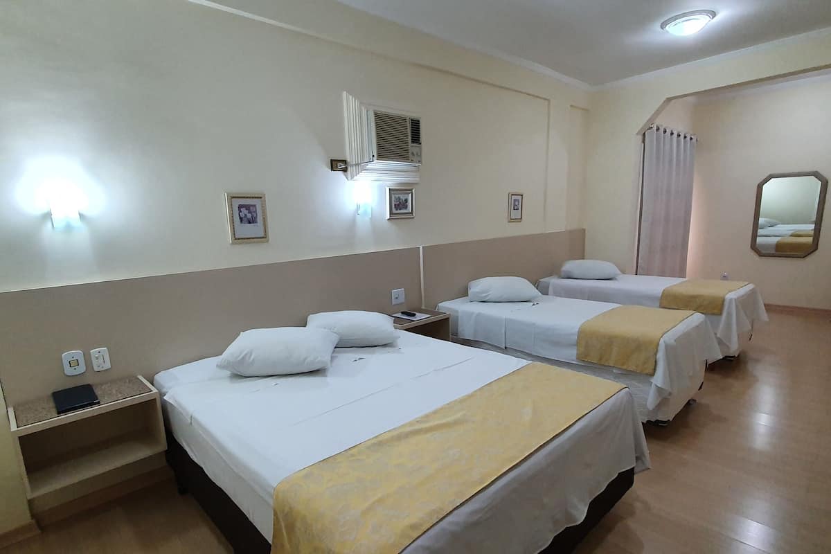 A hotel room with three beds, a bedside table, a nightstand, a wall-mounted mirror, and a ceiling light.
