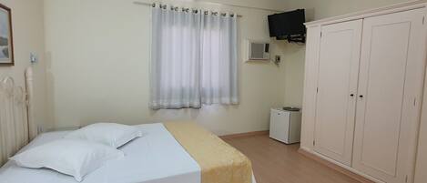 A bedroom with a bed, a wardrobe, a television, and an air conditioning unit.
