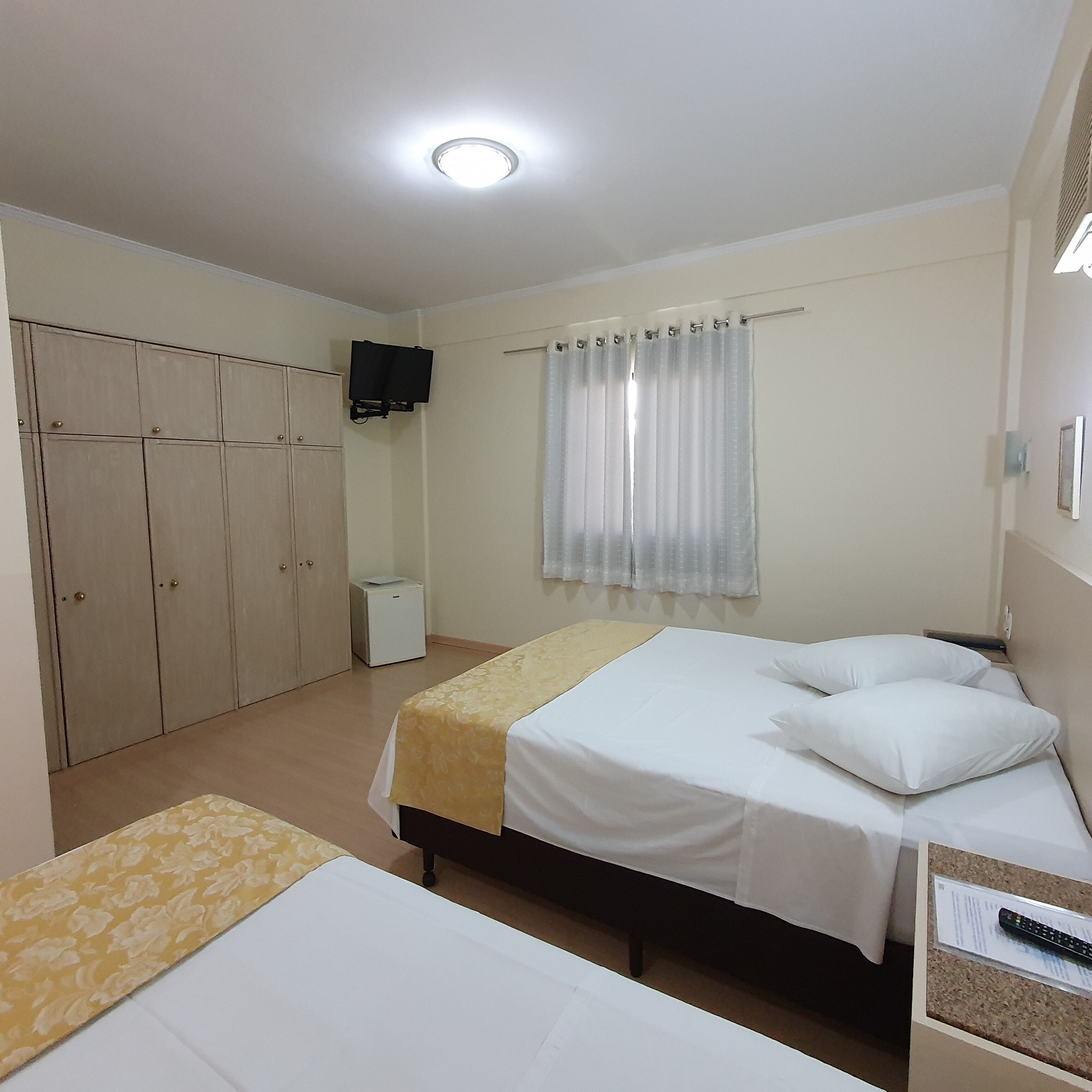 A hotel room with two beds, a wardrobe, a television, and a window with curtains.