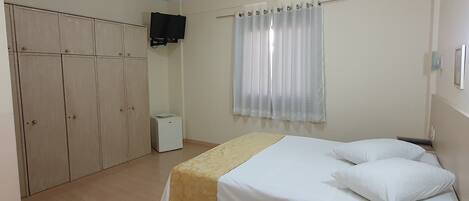 A hotel room with two beds, a wardrobe, a television, and a window with curtains.