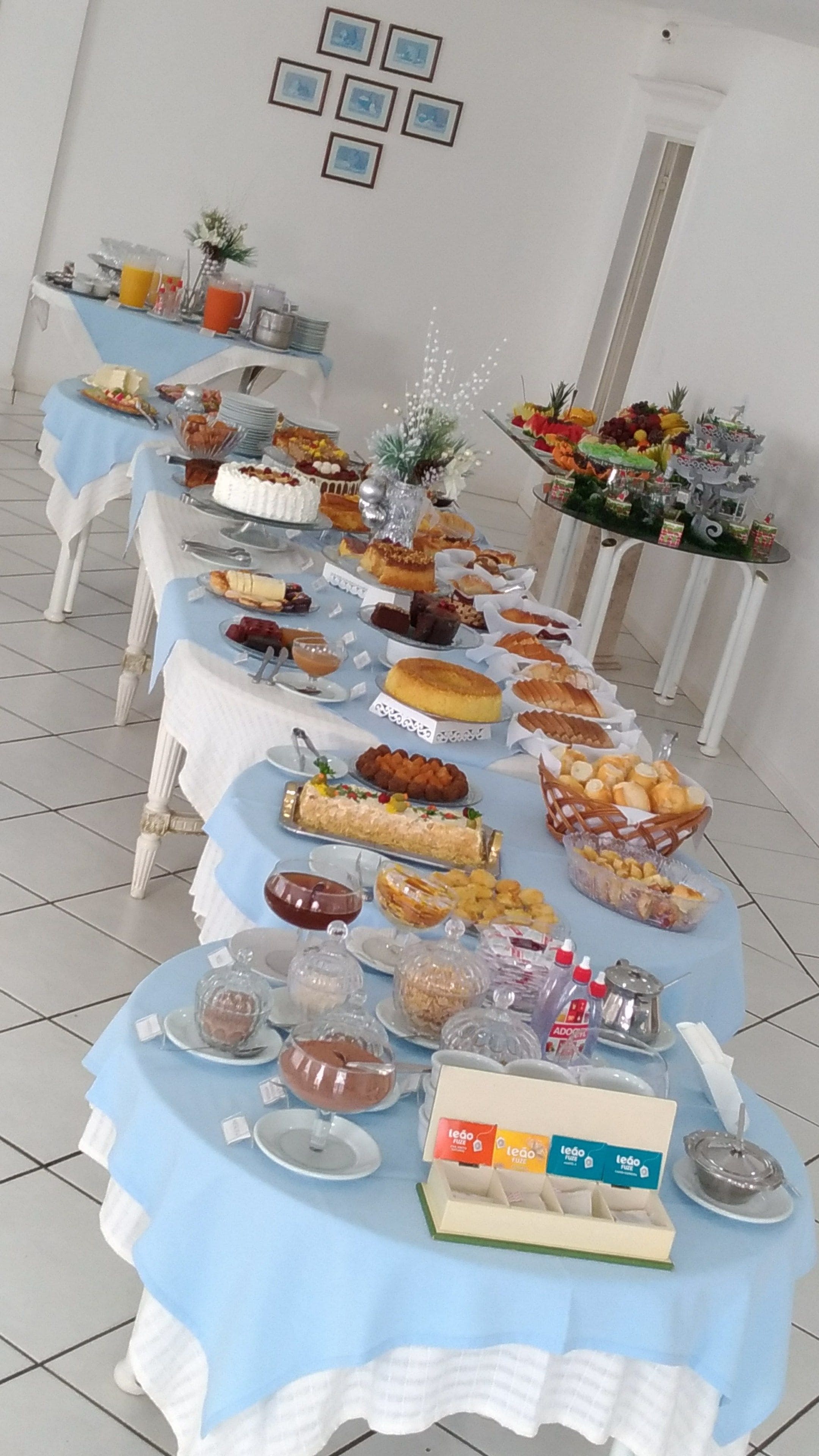 Una mesa de buffet con diversos alimentos y un pastel, dispuesta en una sala con paredes blancas y suelo de baldosas.