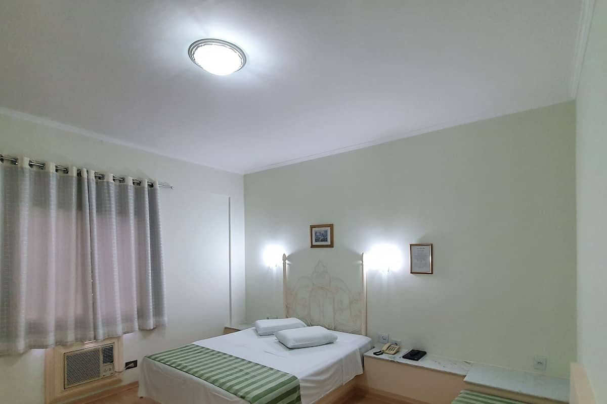 A hotel room with a bed, bedside tables, a telephone, and a radiator.